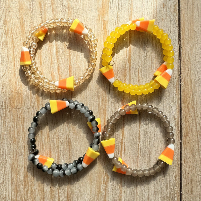 Four beaded stretch bracelets arranged in a 2x2 grid on a dark surface. Each bracelet features candy corn beads 