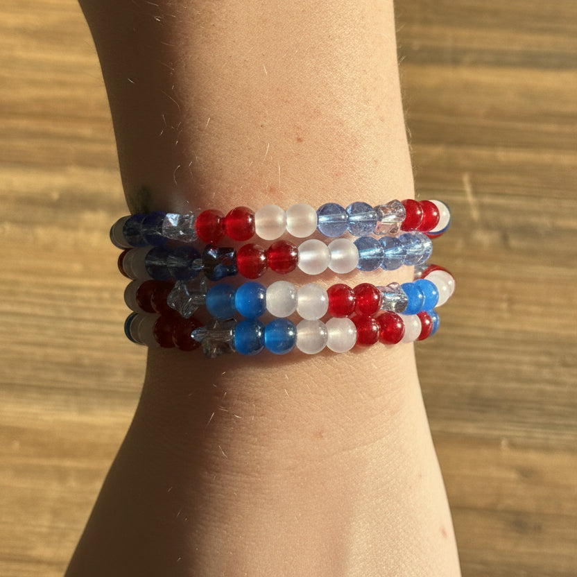 A close-up of a person's wrist wearing a stack of beaded stretch bracelets in red, white, and blue.