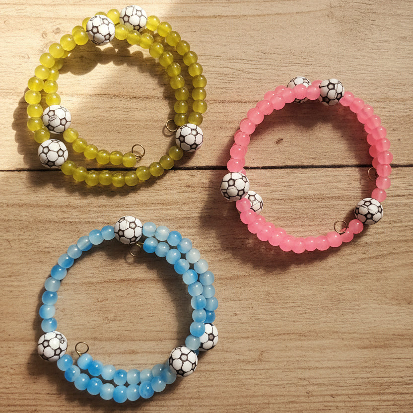 Three beaded stretch bracelets with soccer-ball patterned beads, shown in yellow-green, pink, and light blue