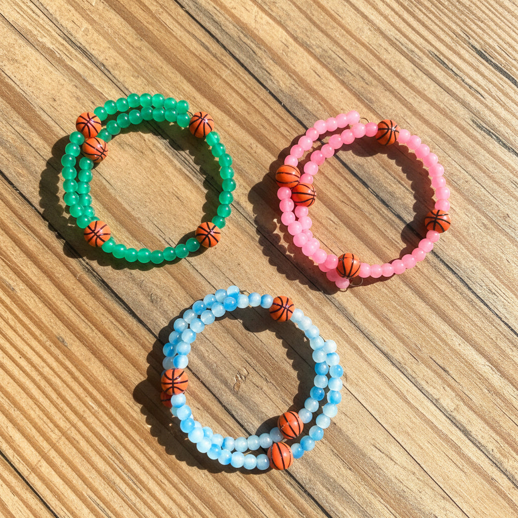 Three beaded stretch bracelets one green, one pink, and one light blue, each accented with small orange basketball beads. 