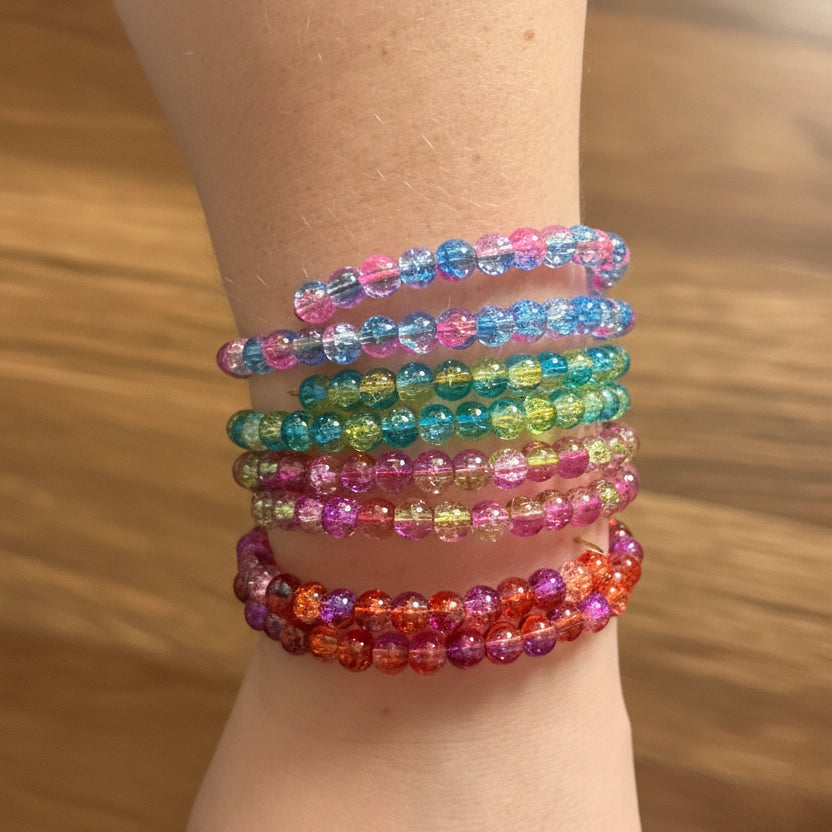 A stack of colorful beaded stretch bracelets worn on a person's wrist, shown against a dark background.