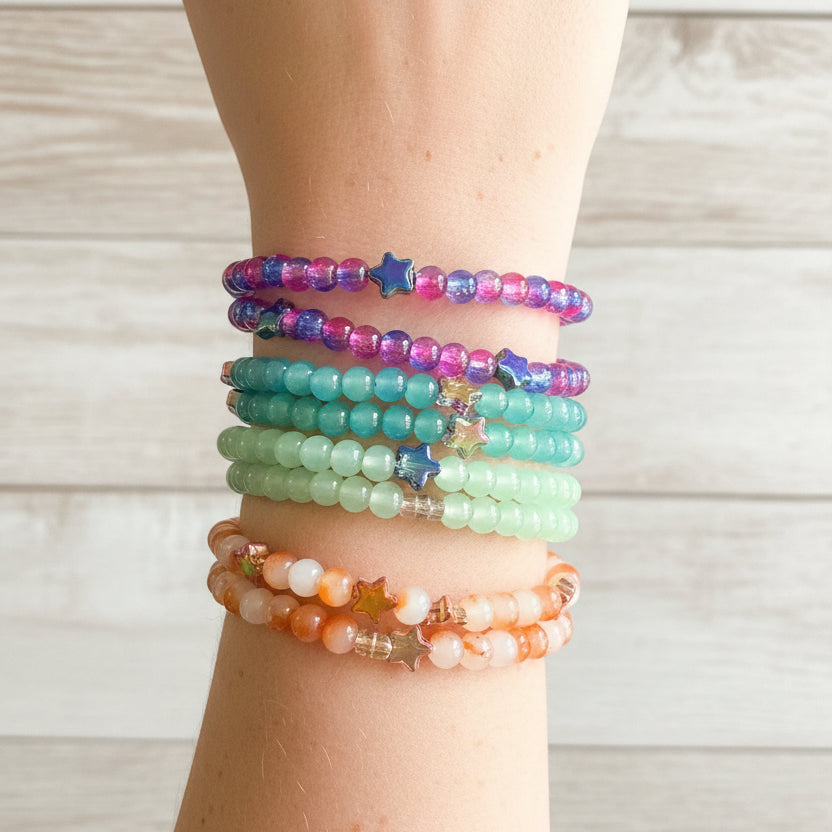 A stack of colorful beaded stretch bracelets worn on a person's wrist. The bracelets feature star-shaped beads and come in pink, blue, green, orange, and white colors