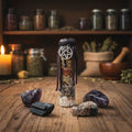 A small glass vial with a black wax seal and silver pentagram pendant, filled with dried herbs and crystals, stands on a tabletop alongside four raw crystals.