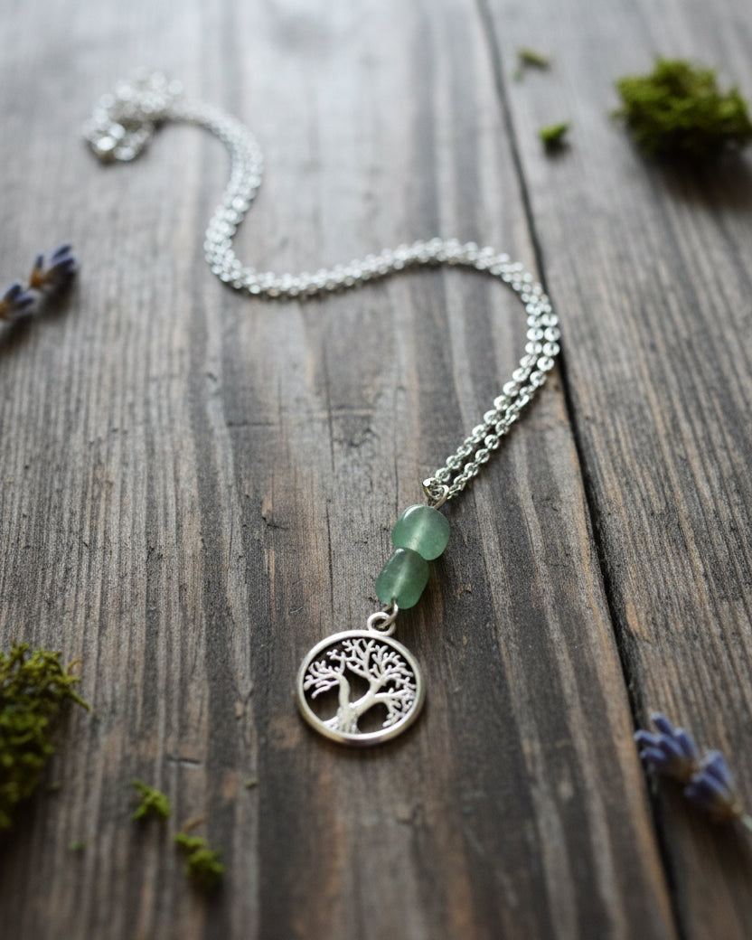 A silver-toned tree of life pendant necklace with a green bead accent, 