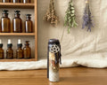 A small glass bottle with a dark wax-sealed cap and a silver pentagram charm, standing on a wooden surface 