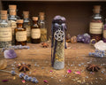 A small bottle with a silver pentagram charm, standing on a wooden tabletop 