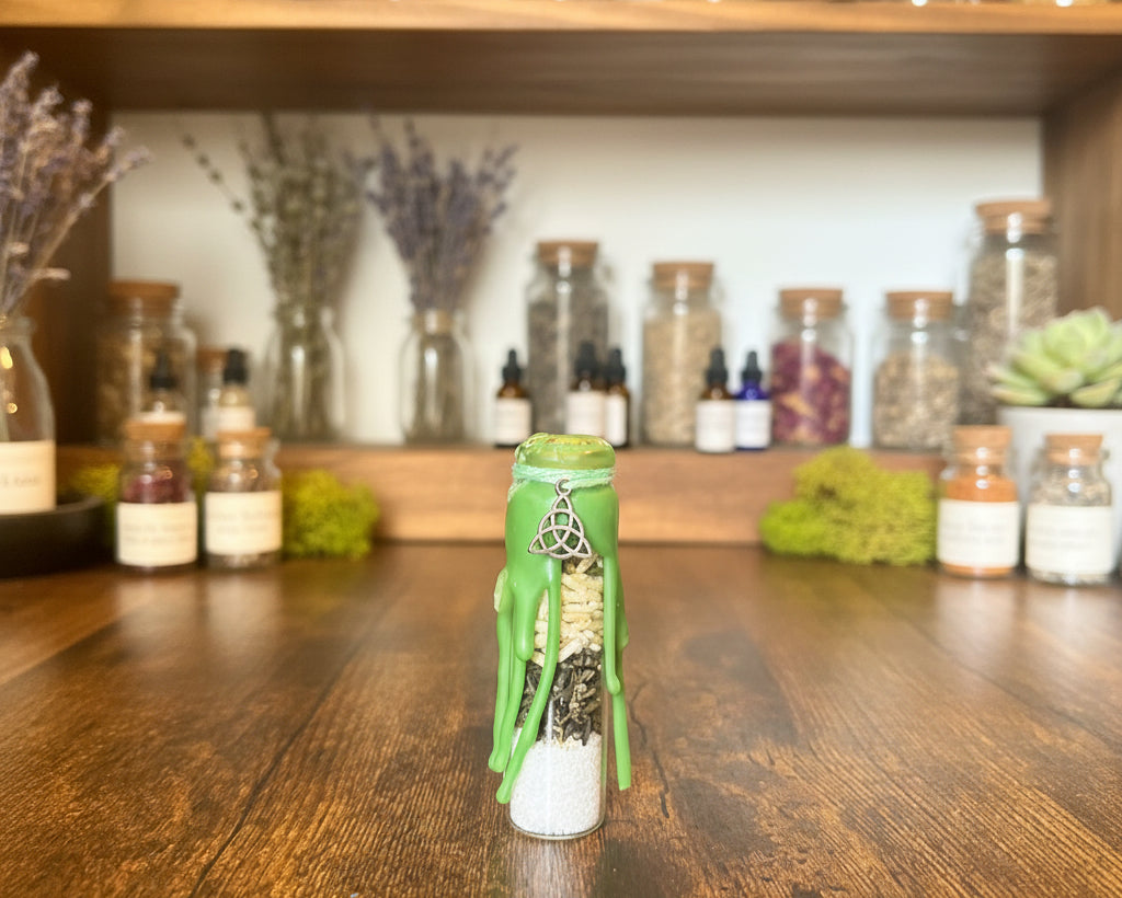 A small glass vial with a green wax seal and a silver charm, containing white powder and dried botanicals, standing on a wooden surface