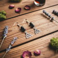 A pair of dangle earrings  The earrings feature three black beads, a silver fishhook ear wire, a silver Celtic knot triquetra charm,