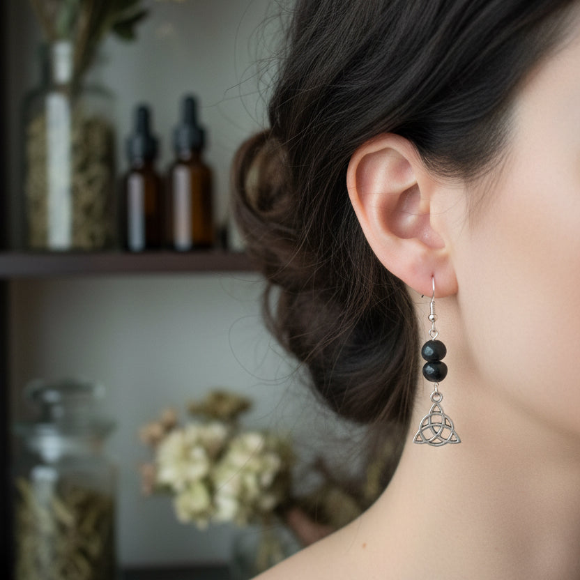 A pair of dangle earrings  The earrings feature three black beads, a silver fishhook ear wire, a silver Celtic knot triquetra charm,