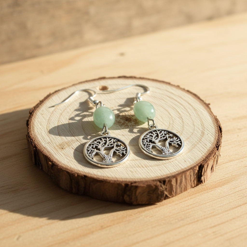 A pair of silver tree-of-life dangle earrings with light green beads, displayed on a round wooden slice