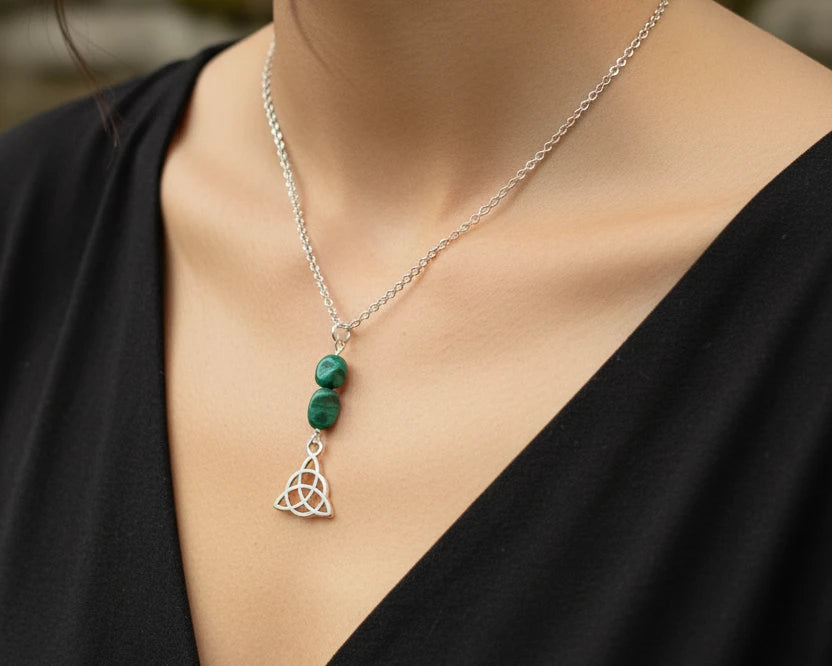 A silver chain necklace featuring two green stone beads and a silver Celtic triquetra pendant,