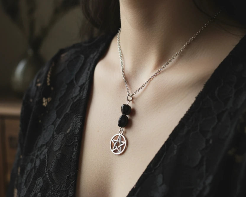 A silver-toned necklace featuring a pentagram pendant and two dark, polished beads on a black background.