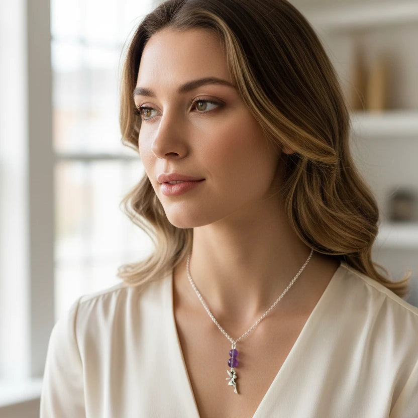 A silver chain necklace featuring two purple faceted beads and a dangling silver fairy charm