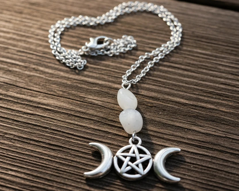 A silver-toned necklace with a three-moon phase pendant and a central pentagram, displayed on a weathered wooden surface .