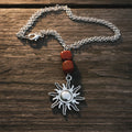 A silver-toned necklace featuring a sun pendant and two red beads, displayed on a weathered wooden surface 