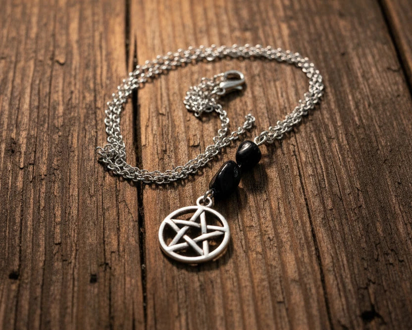 A silver-toned chain necklace with a pentagram pendant and two black beads, displayed on a weathered wooden surface 