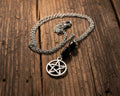A silver-toned chain necklace with a pentagram pendant and two black beads, displayed on a weathered wooden surface 